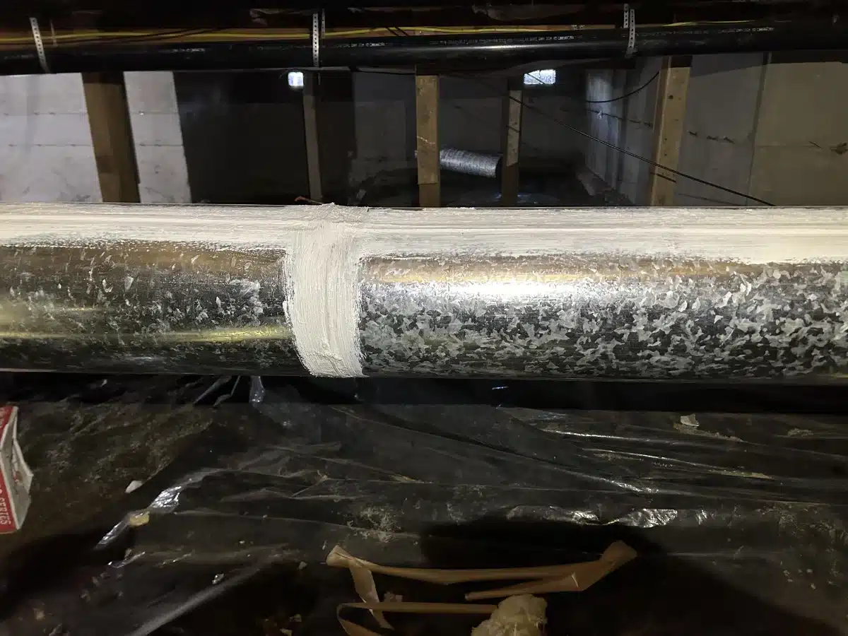 duct-sealing-img-1 Metal pipe with a white sealant joint in a basement/utility area, showing a recent repair.