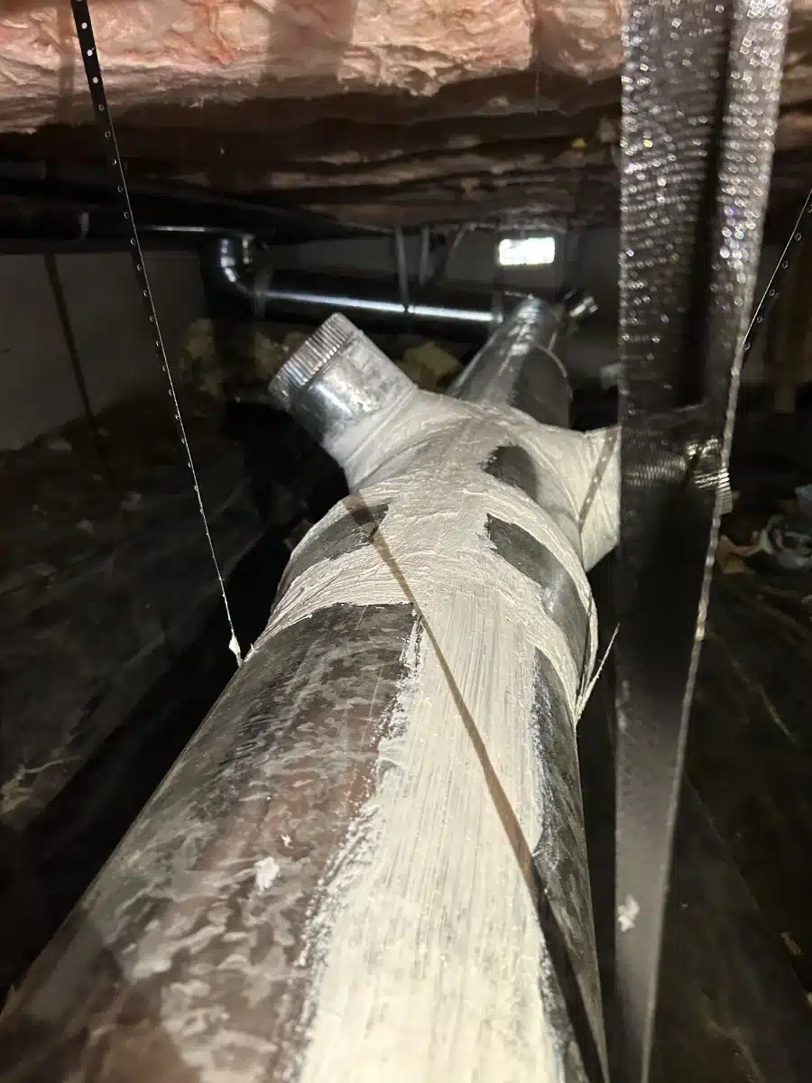 duct-sealing-img-2 Close-up of a metal HVAC duct with a round joint in a dusty basement crawl space.
